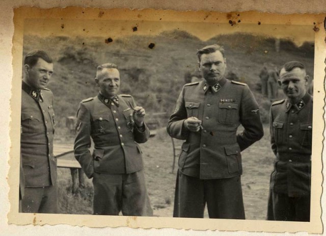 Four S-S officers stand together smiling and chatting in a field. The two in the center are smoking.